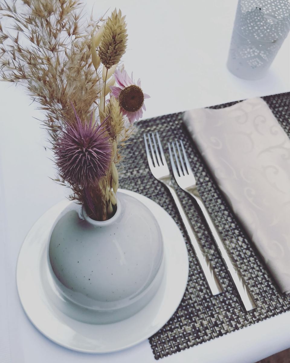 Gedeck mit Stoffserviette, Besteck und Trockenblumen in kleiner Vase