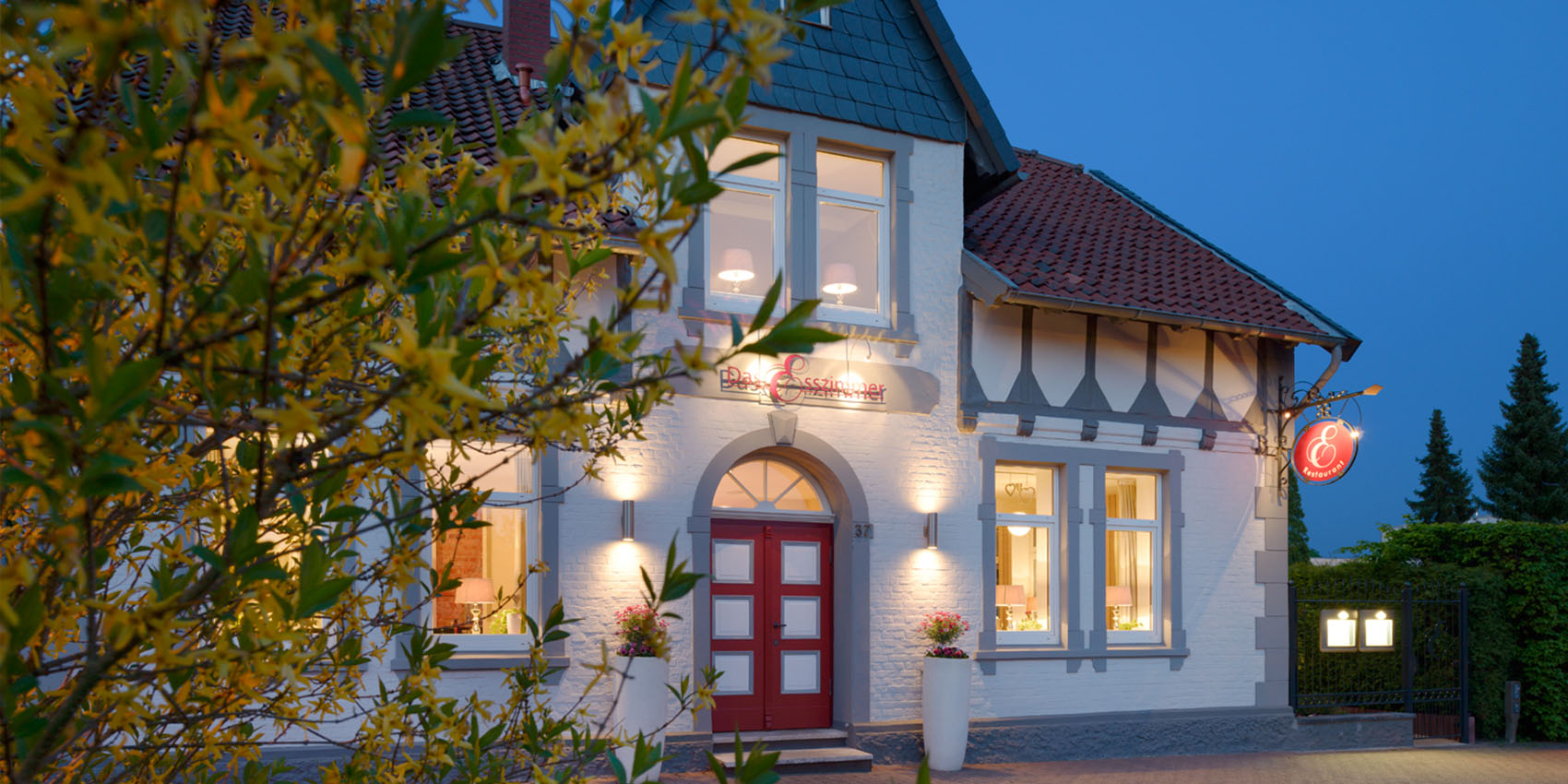 Das Esszimmer in Celle am Abend – beleuchtete Fassade mit roter Eingangstür, Hostmannstraße 37