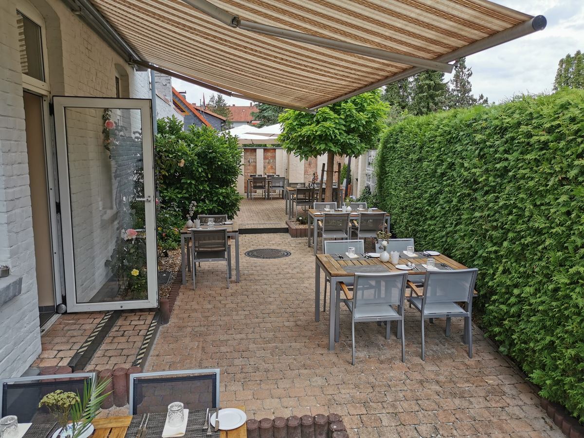 Gartenterrasse unter der Markise mit eingedeckten Tischen entlang der Hecke