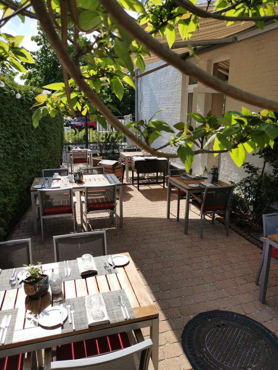 Eingedeckte Tische auf der Terrasse unter berankter Pergola