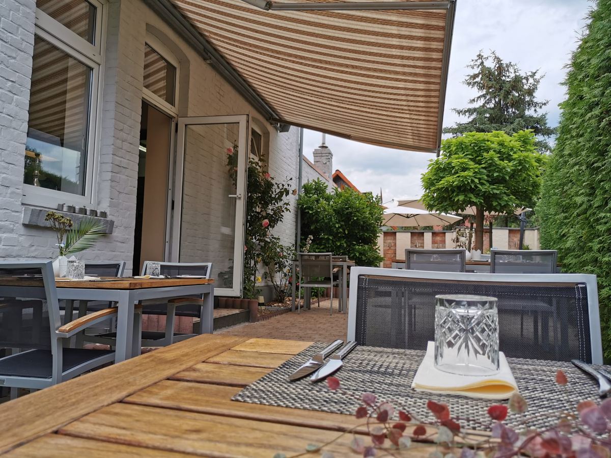 Eingedeckter Tisch auf der Gartenterrasse, dahinter weitere Tische unter der Markise